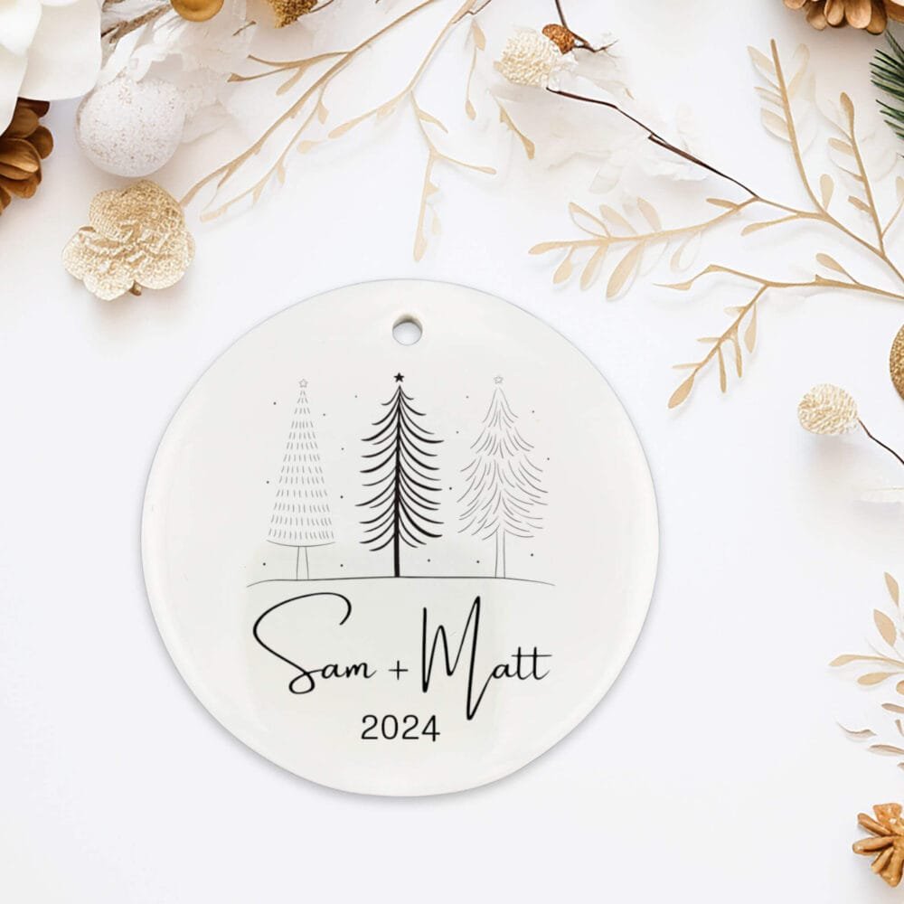 Personalized couple round ornament featuring a minimalist Christmas tree sketch lay down on a table with a couple first names and year.